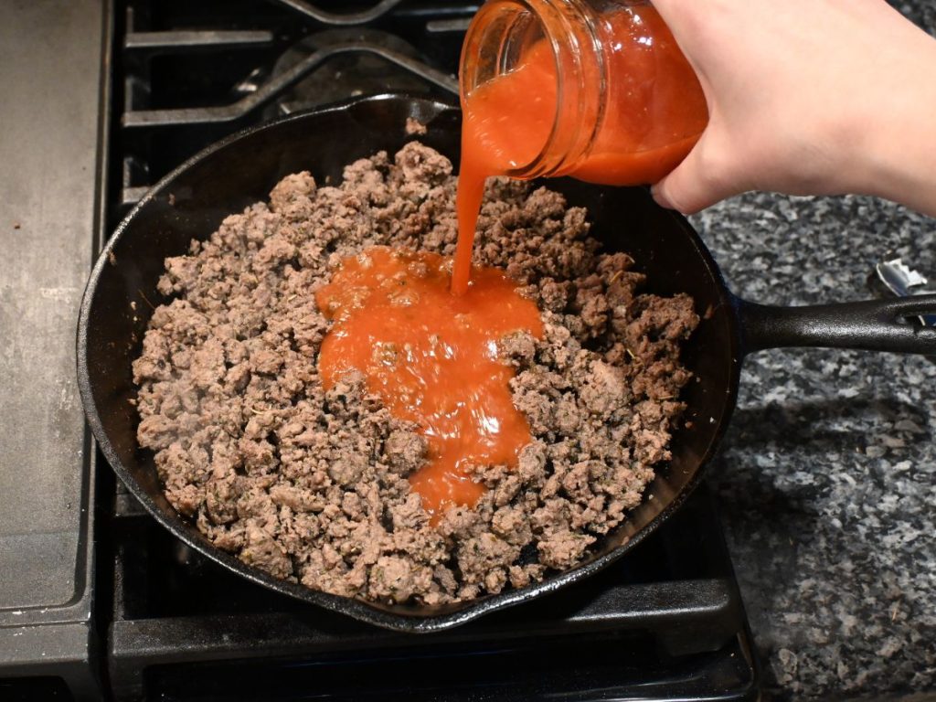woman-pouring-spaghetti-sauce-on-ground-beef