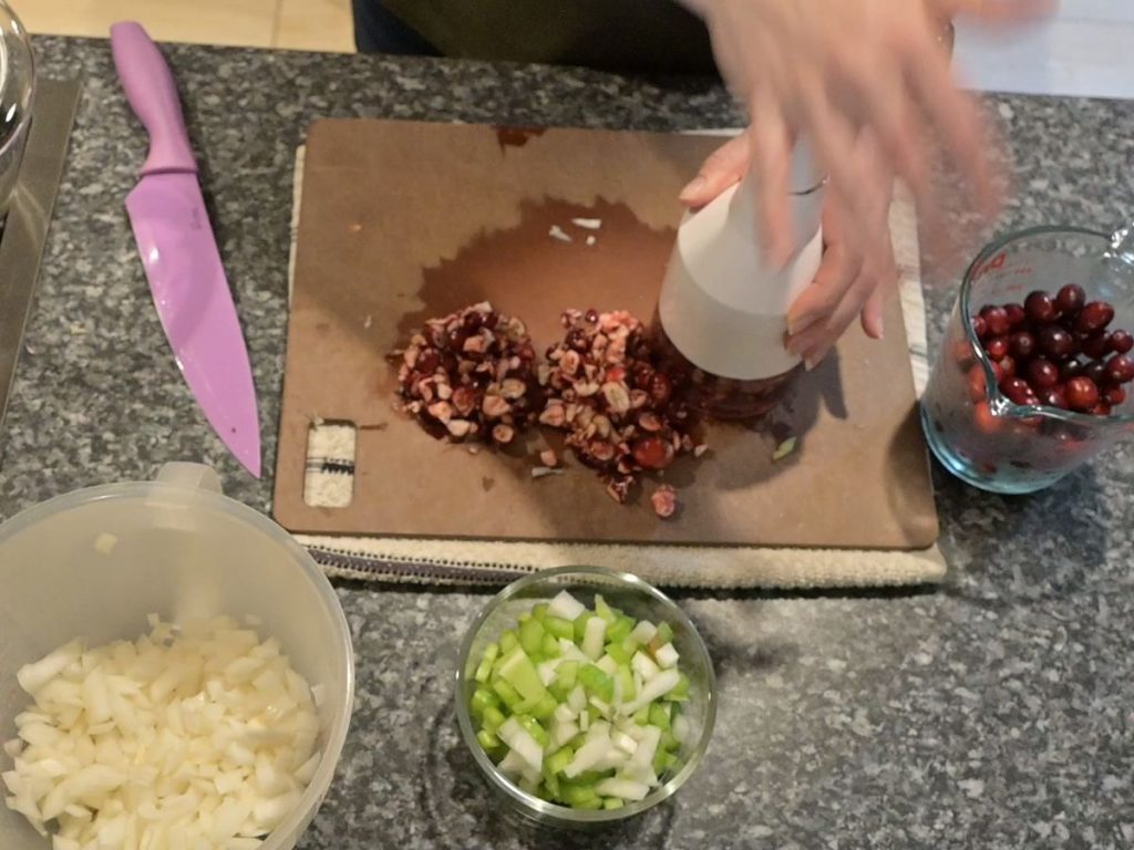chopping cranberries on a cutting board and diced onions and sliced celery