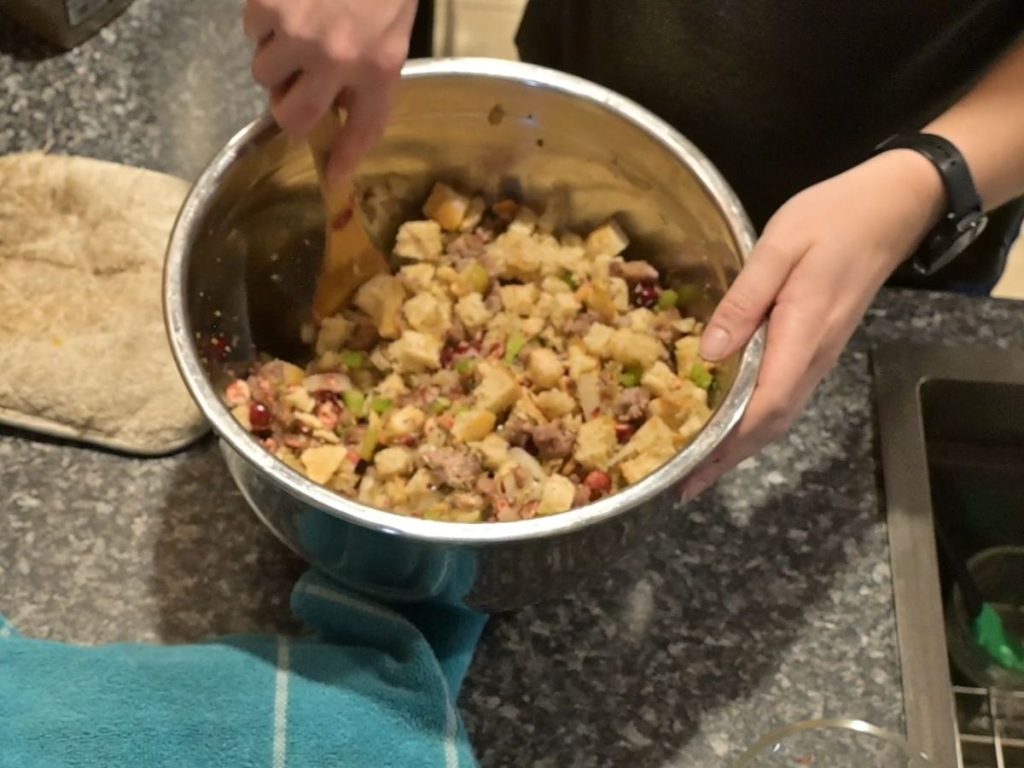 woman mixing sausage and cranberry stuffing ingredients together in a large bowl.