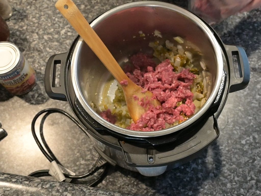 ground beef, green chilis and onions in the instant pot with a wooden spoon